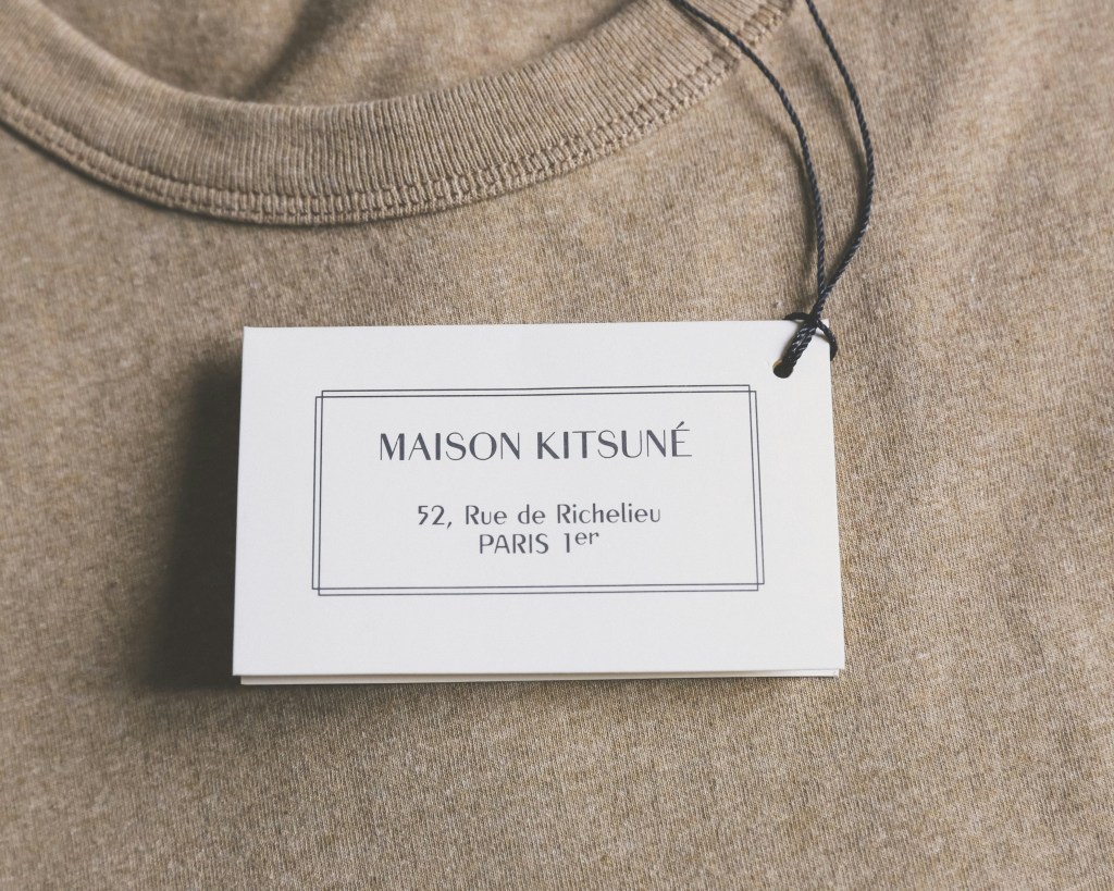 ベージュの洋服に付けられたMaison Kitsuneの白いブランドタグ
